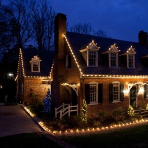 Brick Metro Atlanta home outlined in warm white C9 Christmas lights with lit shrubs and walkway at dusk