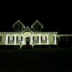 White home with crisp C9 Christmas lights outlining the roofline, dormers, and front porch