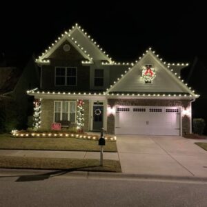 Two-story suburban Georgia home with warm white roofline Christmas lights, lighted wreath, and wrapped entry columns